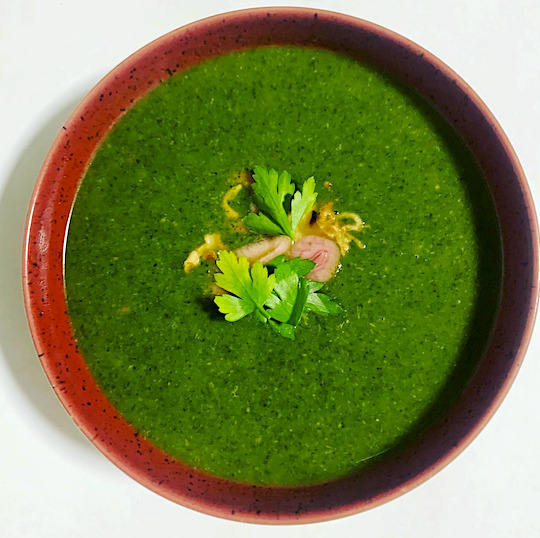 bowl of green soup with carrat shavings and parsley garnish in. a red bowl