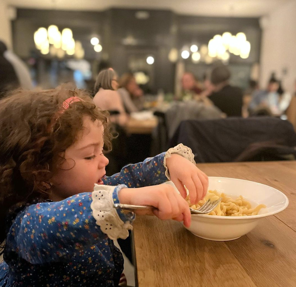 little girl with her hands in the bowl of noodles and a smile on her face