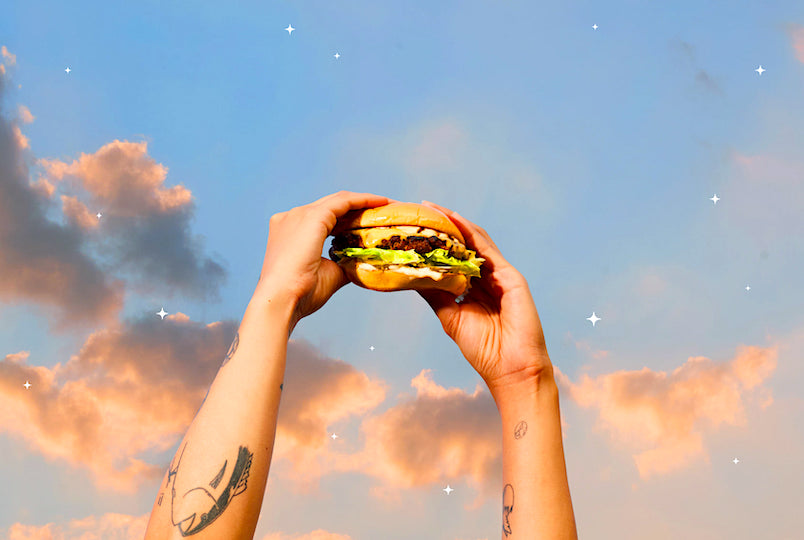 two hands holding a burger with only the sunset background of the sky behind them