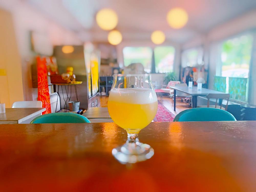 glass of light beer on the wooden bar in focus with a long shot of the rest of the room behind tops and bottom burry