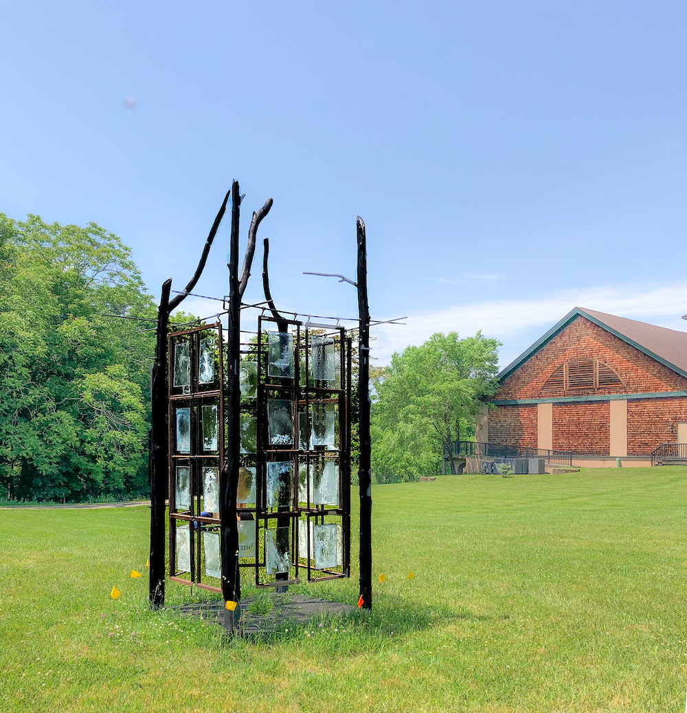 metal sculpture in the grassy lawn with a house in the distance