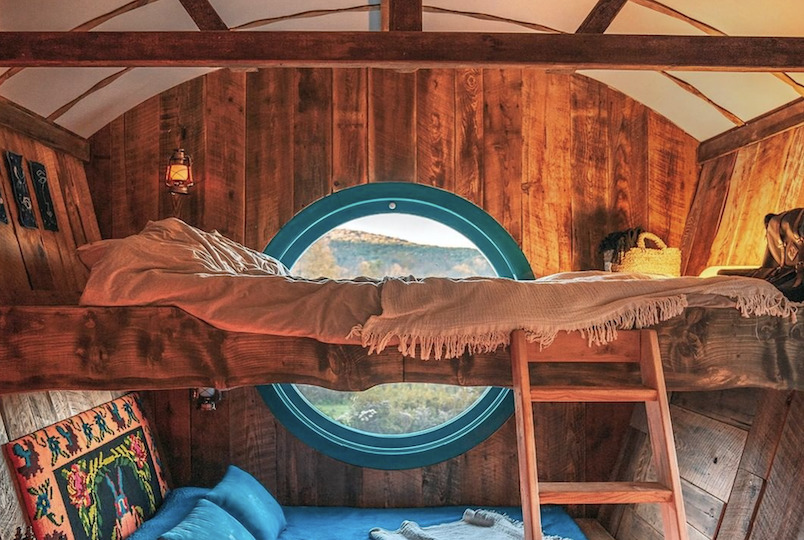 inside of their carnival carriage rental. bed, circle window, ladder, pillows all in bright colors