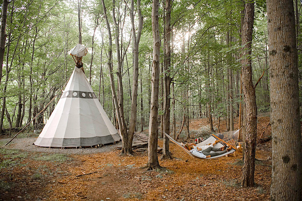 tipi in the woods with a couple of people in a hammock
