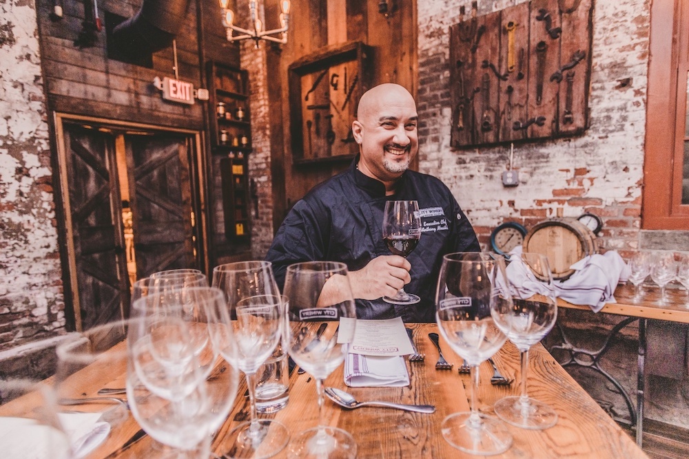 Chef Tony Moustakas drinking wine with a bunch of glasses on the table