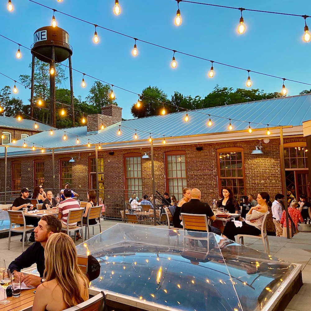 people dining outside on the brick patio during twilight with string lights