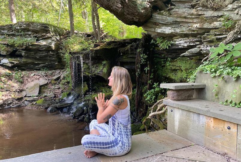 woman doing yoga on stone next to waterfall