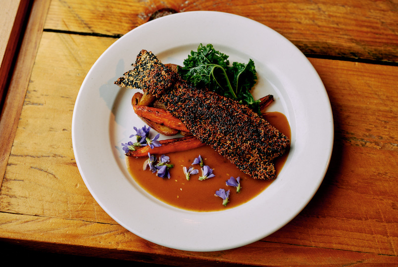 A plate of Sesame seared salmon on a wooden table at Julia's Local restaurant in Round Top NY
