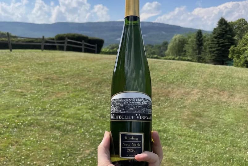 bott;e of white wine being held up to a nature backdrop or field and sky from Whitecliff Vineyard at Hudson in Hudson NY
