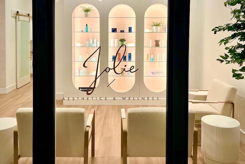 Logo on the window looking though at the inside of the store with Aesthetic products on the shelf at Jolie Aesthetics & Wellness in Poughkeepsie NY