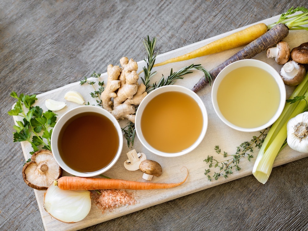 Three different kinds of bone broth on a board with veggies