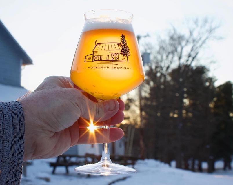 Glass of beer with logo glowing from the sun shining through from Vosburgh Brewing Company & Taproom in Elizavile NY