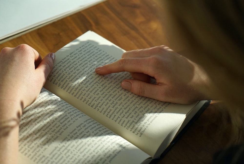 a person reading a book using their finger to follow along for the Community Building Through Volunteers blog by Jenny Wonderling and Inside+Out Upstate NY in the Hudson Valley
